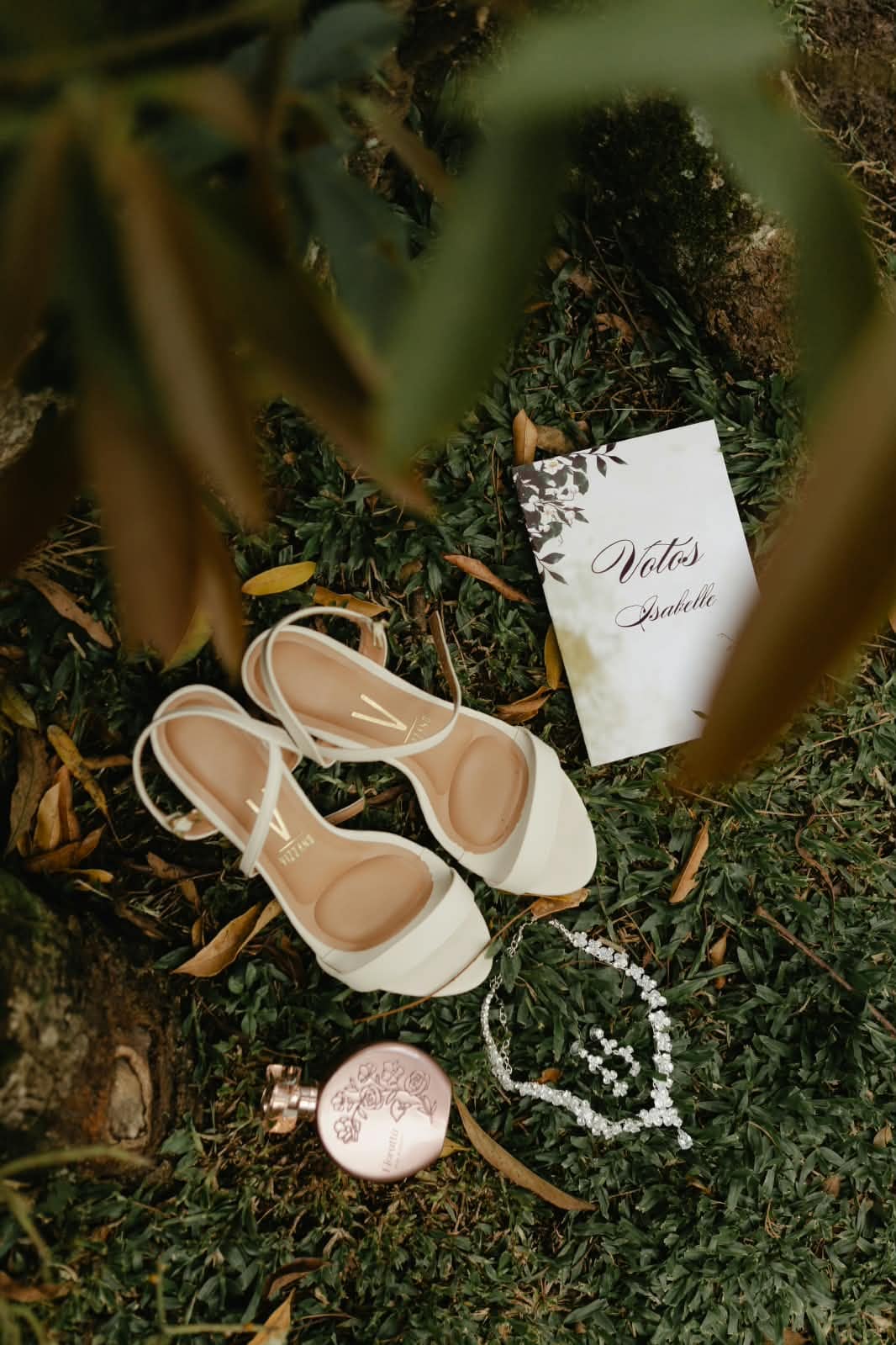 Sapatos da noiva, convite e colar dispostos sobre o gramado